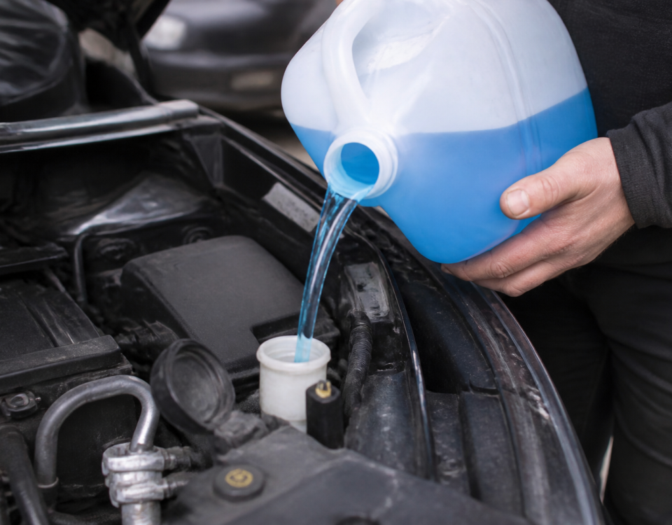 Bidon d'antigel bleu versé dans reservoir automobile ouvert