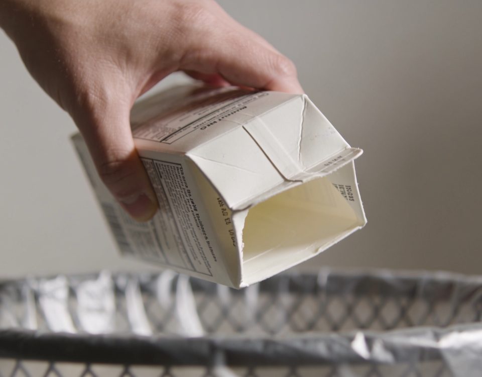 Mains tenant une cartouche de lait vide au-dessus d'une poubelle de recyclage.