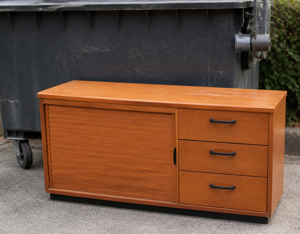 Meuble de bureau en bois posé devant benne a dechets