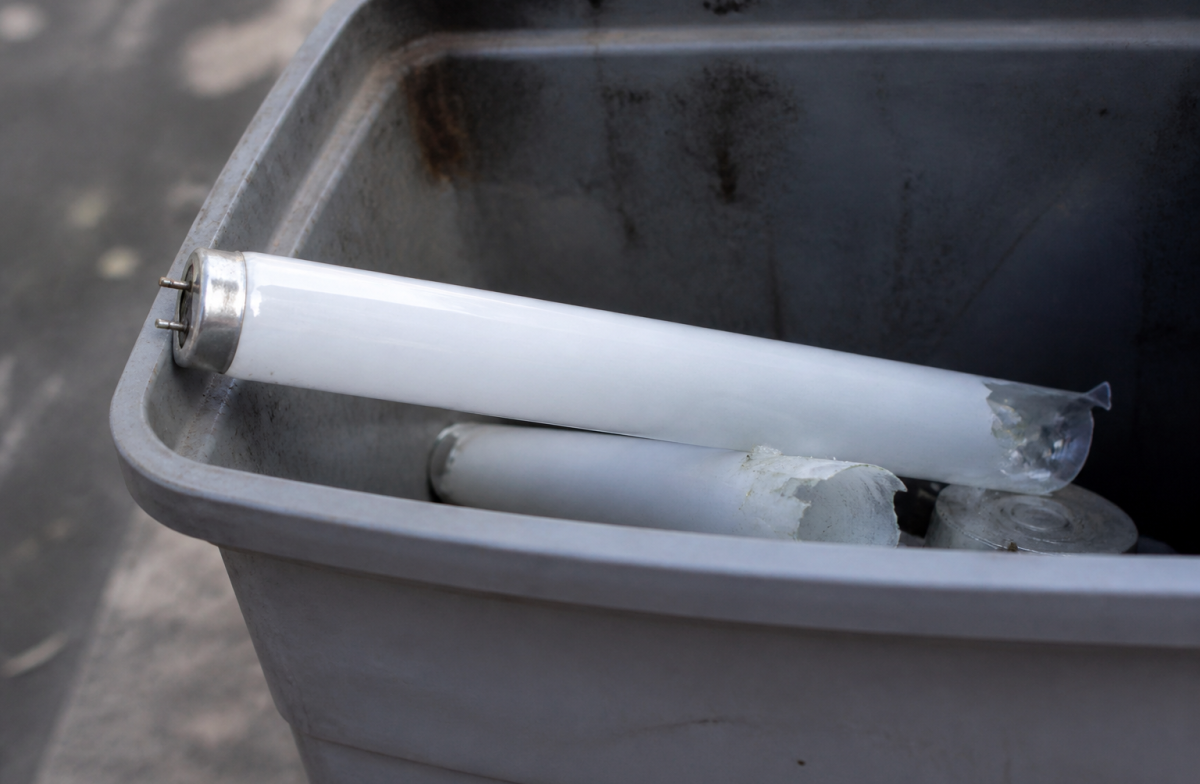 Tube fluorescent cassé posé dans bac recyclage gris.