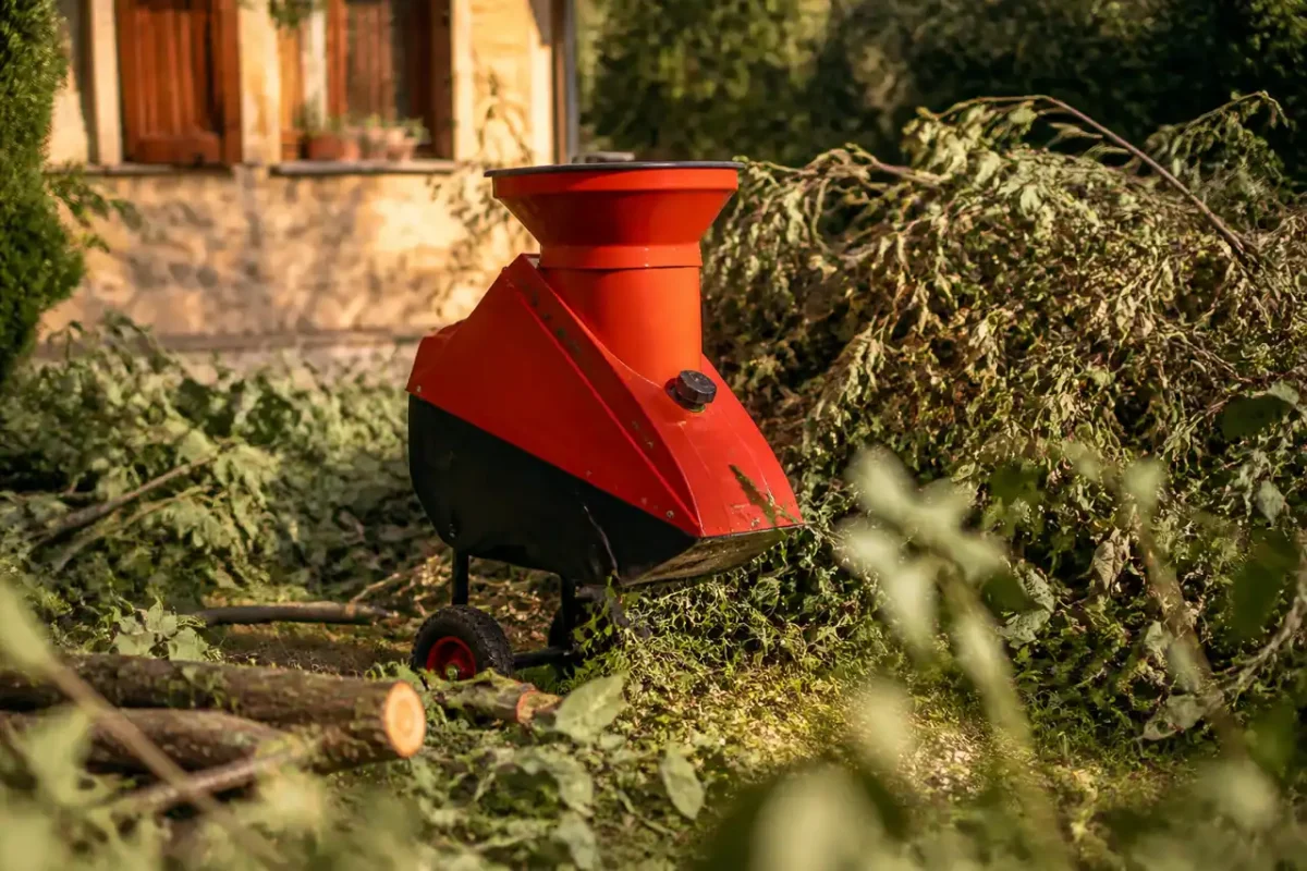 Broyeur de jardin rouge entoure de branches coupees