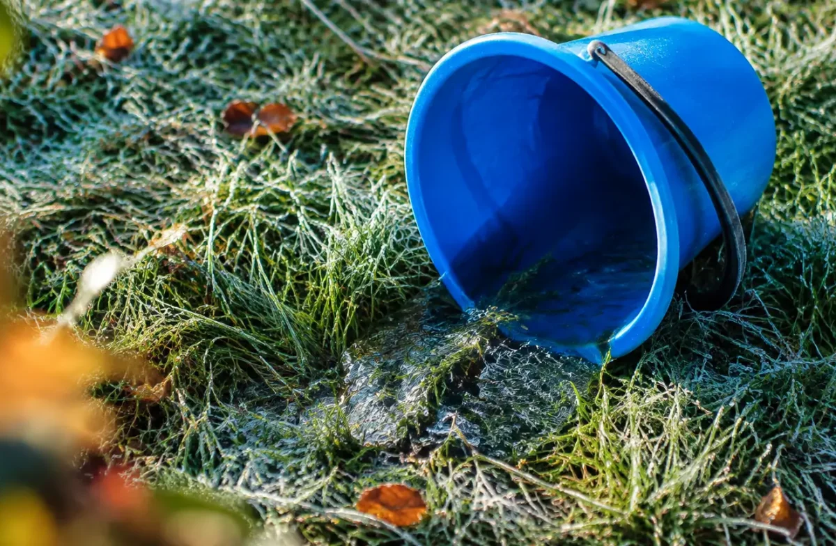 Seau en plastique renverse sur herbe couverte de givre